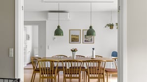 Zona pranzo con tavolo e sedie in legno, due lampade a sospensione e condizionatore d'aria a parete.