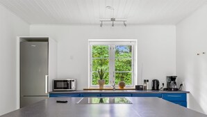 Una cucina moderna con una grande isola, un forno a microonde, una macchina da caffè e una finestra con vista sul verde.