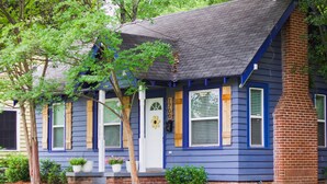A house with a blue exterior, a white front door, and a brick chimney.