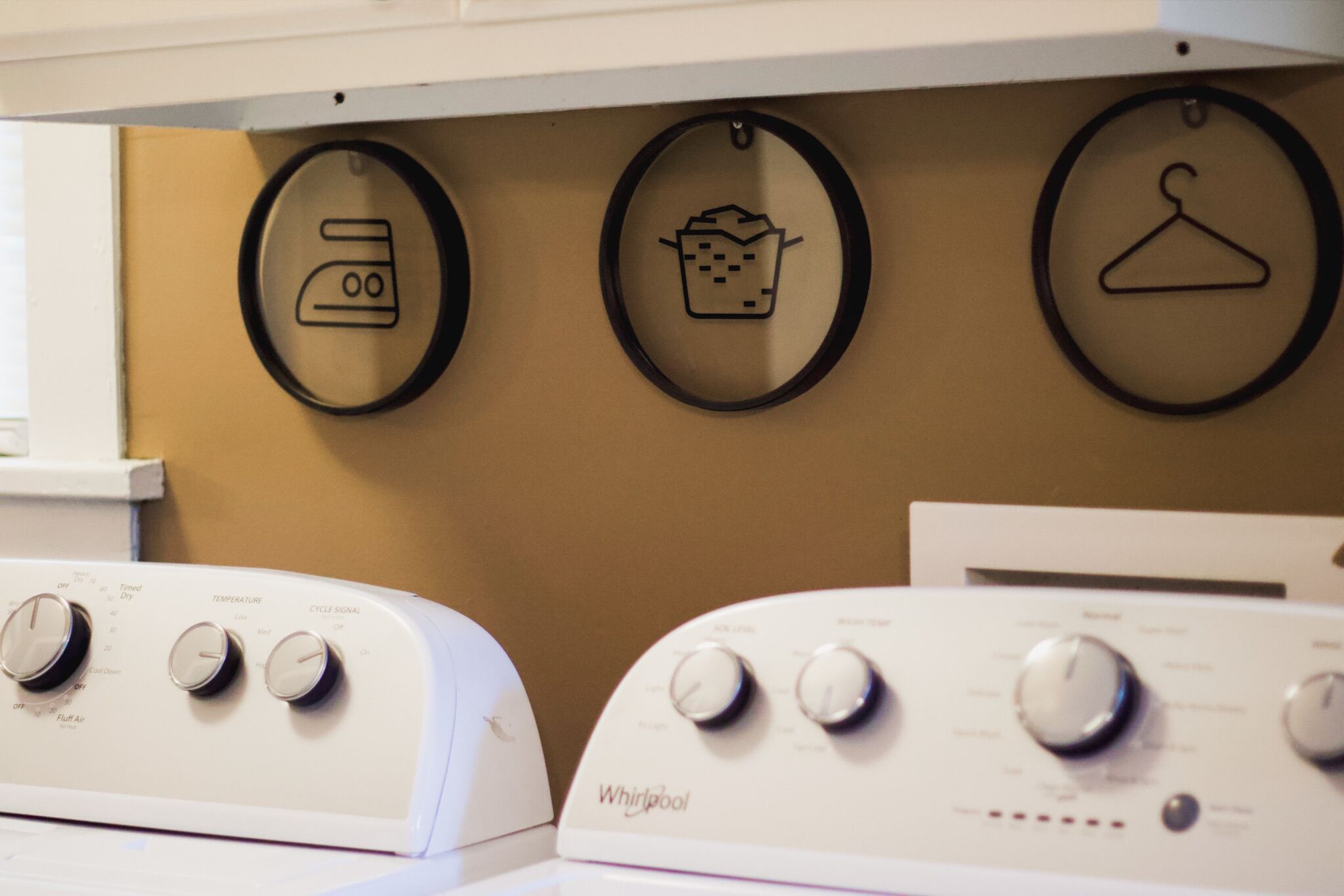 A laundry area with Whirlpool dryers, a wall-mounted dryer, and circular icons indicating laundry functions.