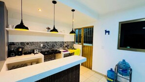 A modern kitchen with a white countertop, black and yellow pendant lights, a tiled backsplash, and a window with a view.