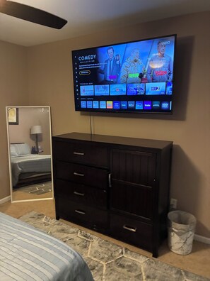 A bedroom with a TV mounted on the wall, a dresser, a bed, and a mirror. - Stunning 5-BedroomHome with Space,Style & Comfort (Fairburn)