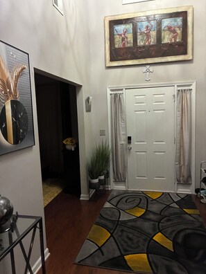 A hallway with a door, a framed painting, a mirror, and a patterned rug. - Stunning 5-BedroomHome with Space,Style & Comfort (Fairburn)