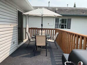 Une terrasse couverte avec une table et des chaises, un barbecue et une rambarde en bois.