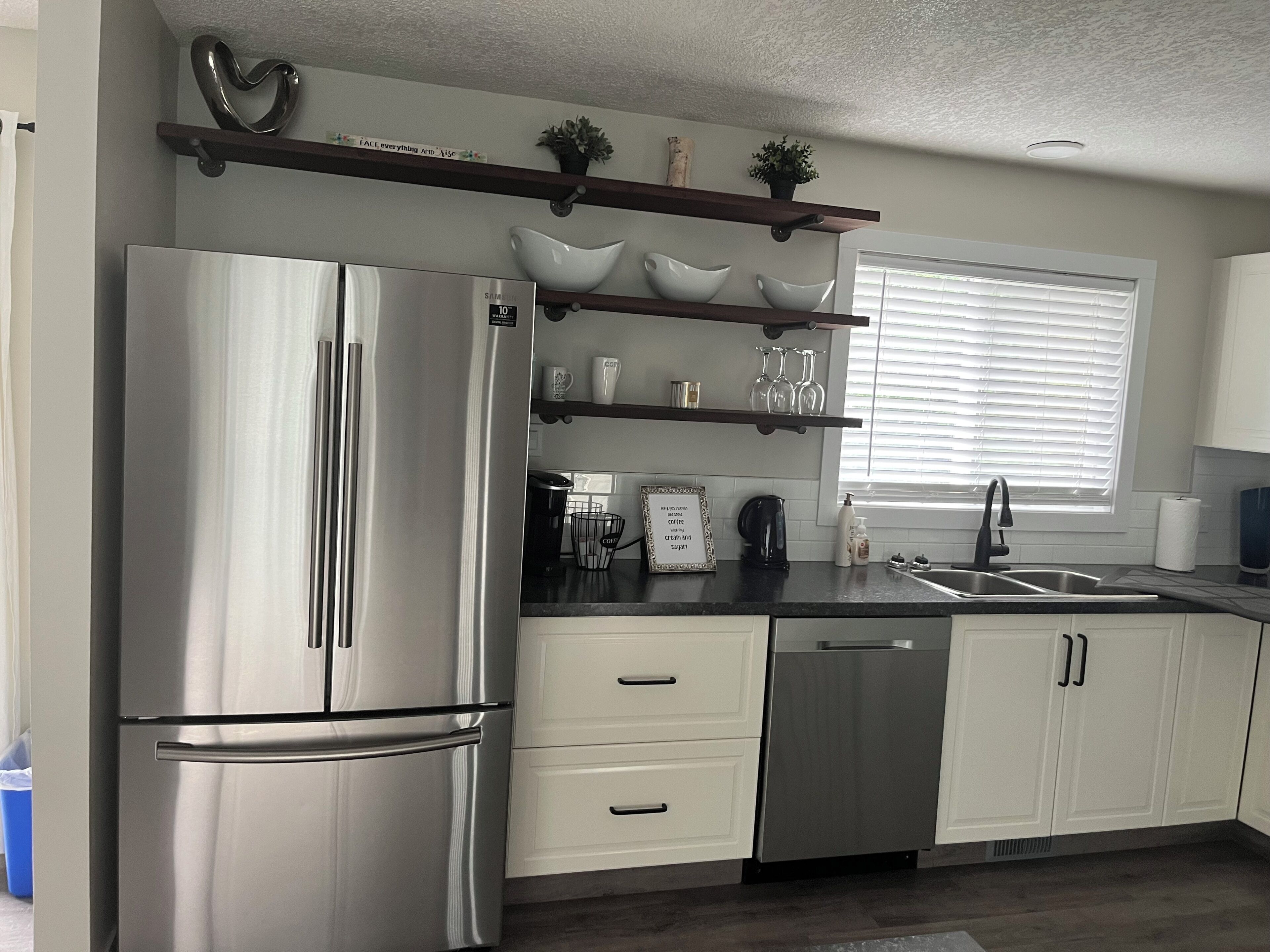 A modern kitchen with stainless steel appliances, white cabinetry, and a window with blinds.