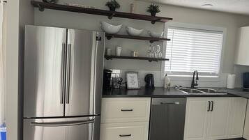 A modern kitchen with stainless steel appliances, white cabinetry, and a window with blinds.