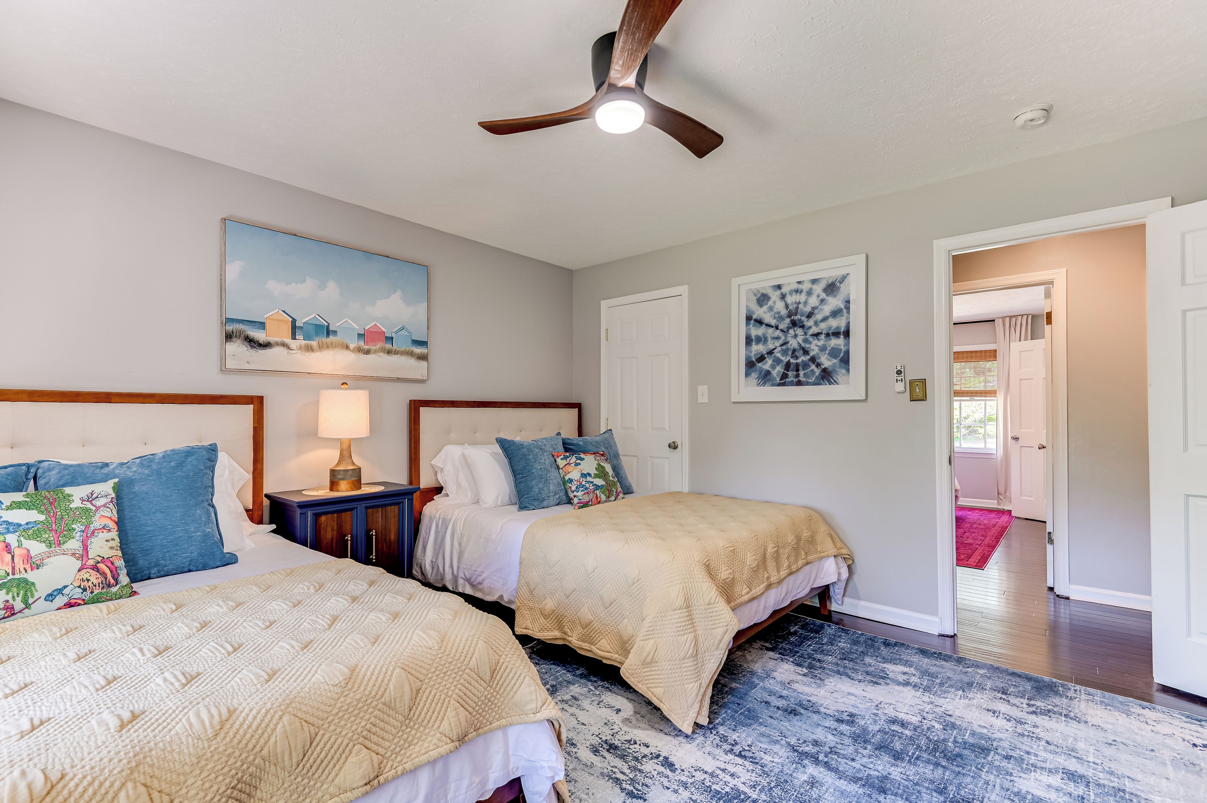 A bedroom with two beds, a ceiling fan, a nightstand, and artwork on the walls.