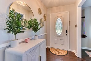 A hallway with a white door, potted plants, a round mirror, and a doormat. - Tropical Papaya -3-BR house in National Hills Augusta/Hot Tub/Pool Table/Yard (Augusta)