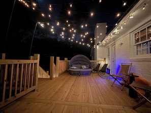 A wooden deck with string lights, a covered seating area, and a white building with windows. - Tropical Papaya -3-BR house in National Hills Augusta/Hot Tub/Pool Table/Yard (Augusta)
