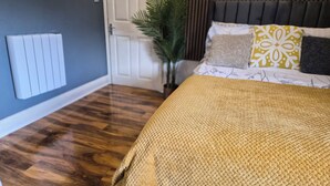 A bedroom with a wooden floor, a bed with a yellow blanket, and a white radiator. - 3 min walk to tube for central London (London)