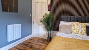 A bedroom with a radiator, a door, a plant, and a bed with patterned pillows. - 3 min walk to tube for central London (London)