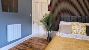 Ein Schlafzimmer mit Heizkörper, Tür, einer Pflanze und einem Bett mit gemusterten Kissen.