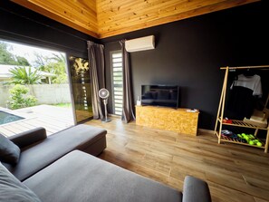 Ein modernes Wohnzimmer mit Fernseher, Holzboden und Pool im Freien.