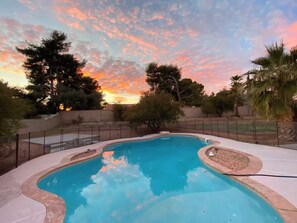 Una piscina de borde curvo, rodeada por una valla y jardines.