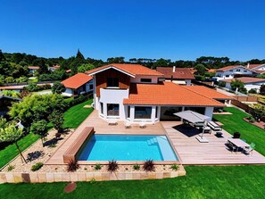 A modern house with a swimming pool, deck, and surrounding greenery. - VILLA LES 3 CHENES avec piscine chauffée face aux Pyrénées (HOSSEGOR)