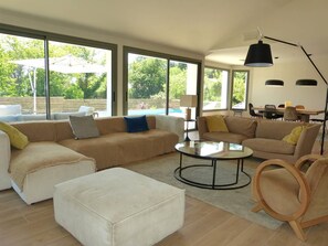 Ein geräumiges Wohnzimmer mit großem Fenster und rundem Couchtisch, mit Blick auf einen Pool.