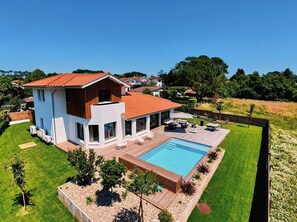 Ein modernes, zweistöckiges Haus mit Swimmingpool, umgeben von einem gepflegten Rasen und Bäumen.