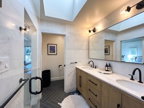 A modern bathroom with a large mirror, dual sinks, and a black trash bin. - Sunny Designer Mill Valley Home; great for kids, walk to park, downtown & trails (Mill Valley)