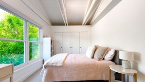 A bedroom with a large window, a bed with a quilt, a bedside table with a lamp, and a wardrobe. - Sunny Designer Mill Valley Home; great for kids, walk to park, downtown & trails (Mill Valley)