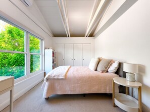A bedroom with a large window, a bed with a quilt, a bedside table with a lamp, and a wardrobe. - Sunny Designer Mill Valley Home; great for kids, walk to park, downtown & trails (Mill Valley)