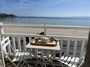 Ein Balkon mit einem für Tee gedeckten Tisch, mit Blick auf einen Strand und ein ruhiges Meer.