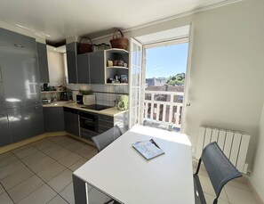 Eine moderne Küche mit grauen Schränken, einem Esstisch mit einem Stuhl und Blick auf Gebäude durch ein Fenster.