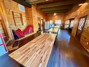 A wooden interior with a long dining table, a refrigerator, and a bench with red cushions. - Camp Coleman-Theater Room - Game Room - Sleeps 29 (Oakhurst)