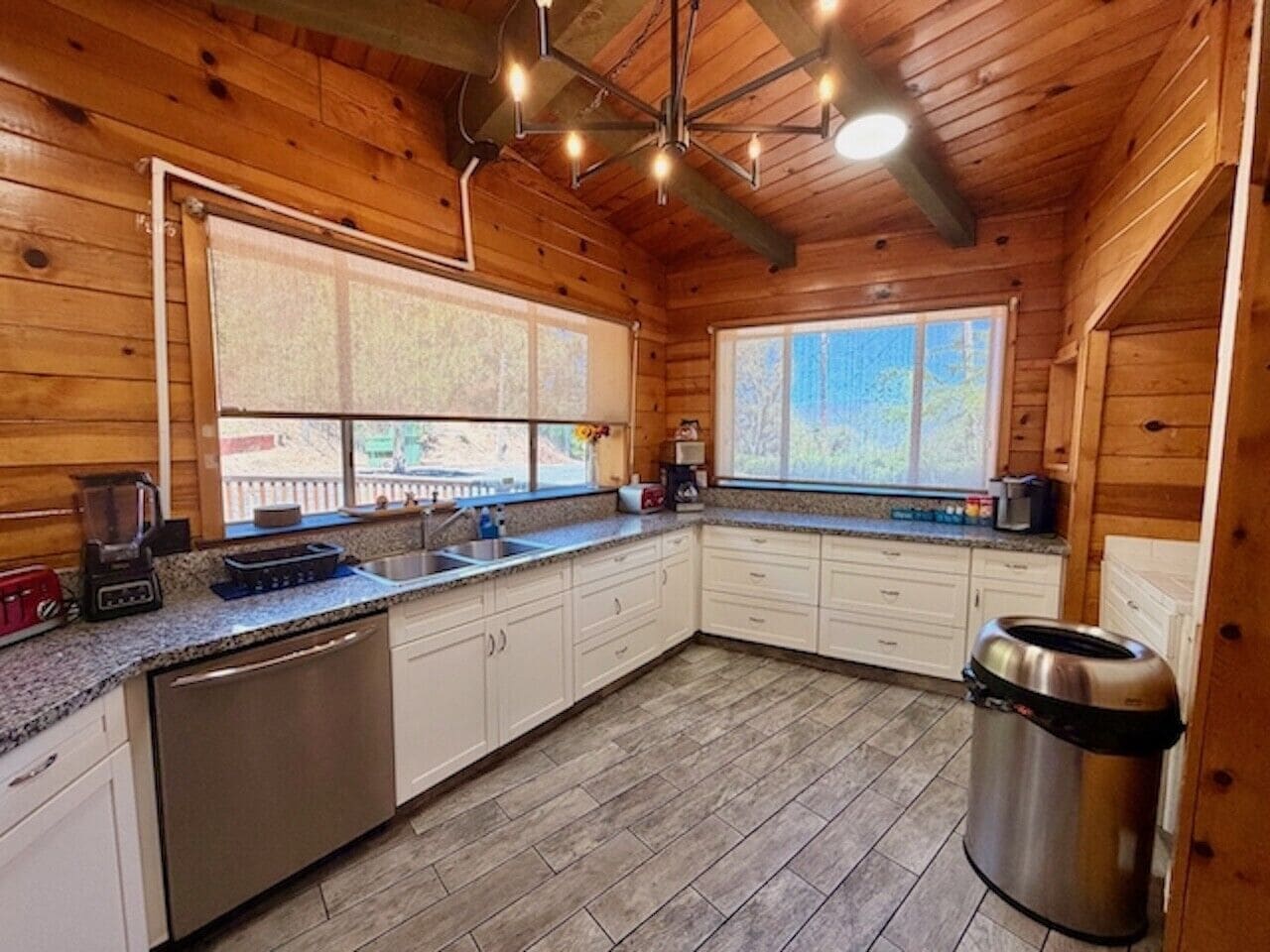 A kitchen with wooden walls, a granite countertop, stainless steel appliances, and a window with a view.