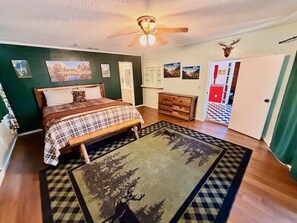 A bedroom with a bed, a dresser, a ceiling fan, and a rug with a forest design. - Camp Coleman-Theater Room - Game Room - Sleeps 29 (Oakhurst)