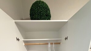 Un armario blanco con un estante de madera, un pequeño adorno verde, un bolso estampado y una cesta blanca para ropa.