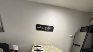 Cocina compacta con encimera de granito, muebles de color blanco y electrodomésticos de acero inoxidable, incluyendo un refrigerador y un microondas.