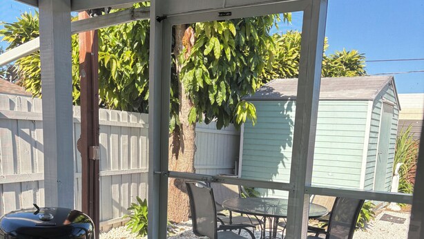 A covered patio with a grill, outdoor seating, and a view of a backyard with a shed and plants. - 3-bedroom apartment in peaceful Stuart with cool AC (Stuart)