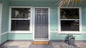 A house with a dark gray front door, two windows, a welcome mat, and a potted plant. - 3-bedroom apartment in peaceful Stuart with cool AC (Stuart)