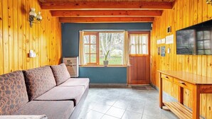 A wooden interior with a sofa, a television, and a window with a view of trees. - Family bungalow : Garden and barbecue : Playa Bonita Bariloche (San Carlos de Bariloche)