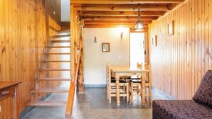 A wooden interior with a staircase, a dining area with a table and chairs, and a sofa. - Family bungalow : Garden and barbecue : Playa Bonita Bariloche (San Carlos de Bariloche)