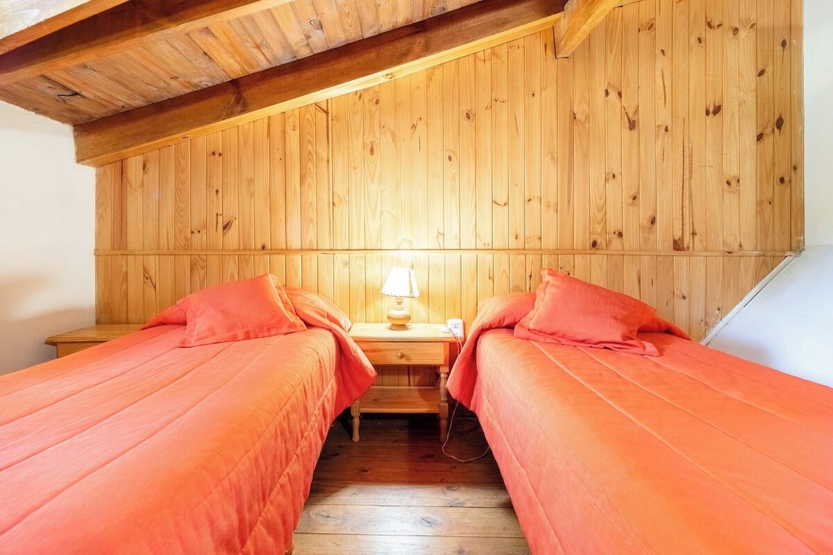 Une chambre avec deux lits, des murs en bois, une table de chevet avec une lampe et un plafond en pente.