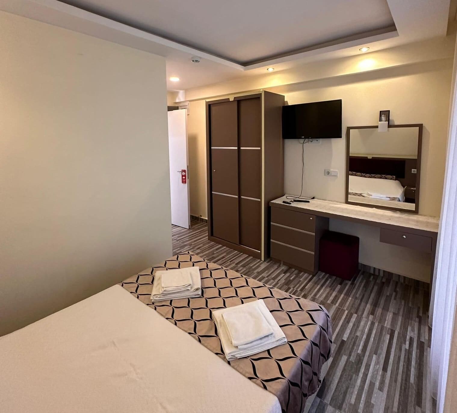 Una habitación de hotel con cama, escritorio con espejo, televisor y armario.