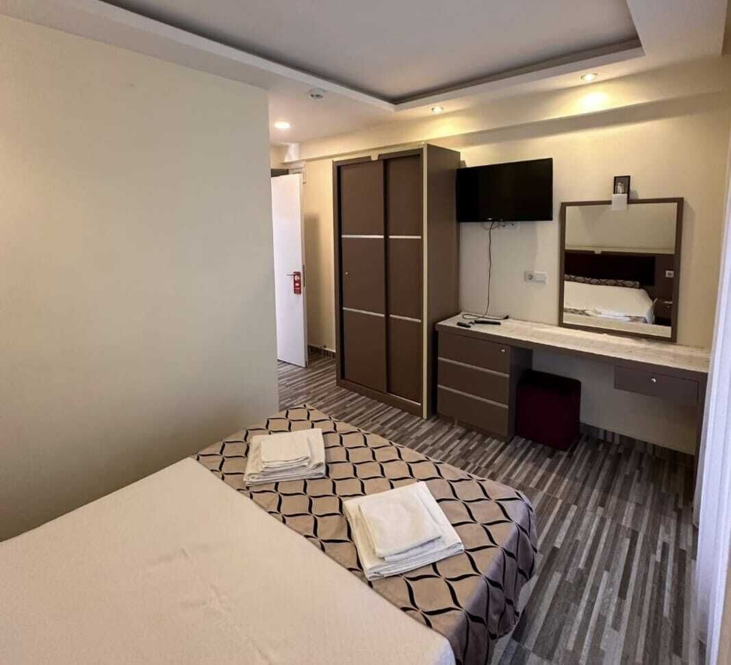 A hotel room with a bed, a desk with a mirror, a wardrobe, and a television.