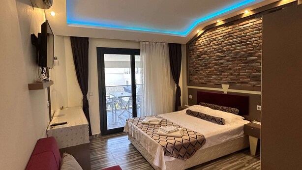 Una habitación de hotel moderna con una cama, un sofá rojo, una mesita y un televisor de pared, además de un balcón con vistas.