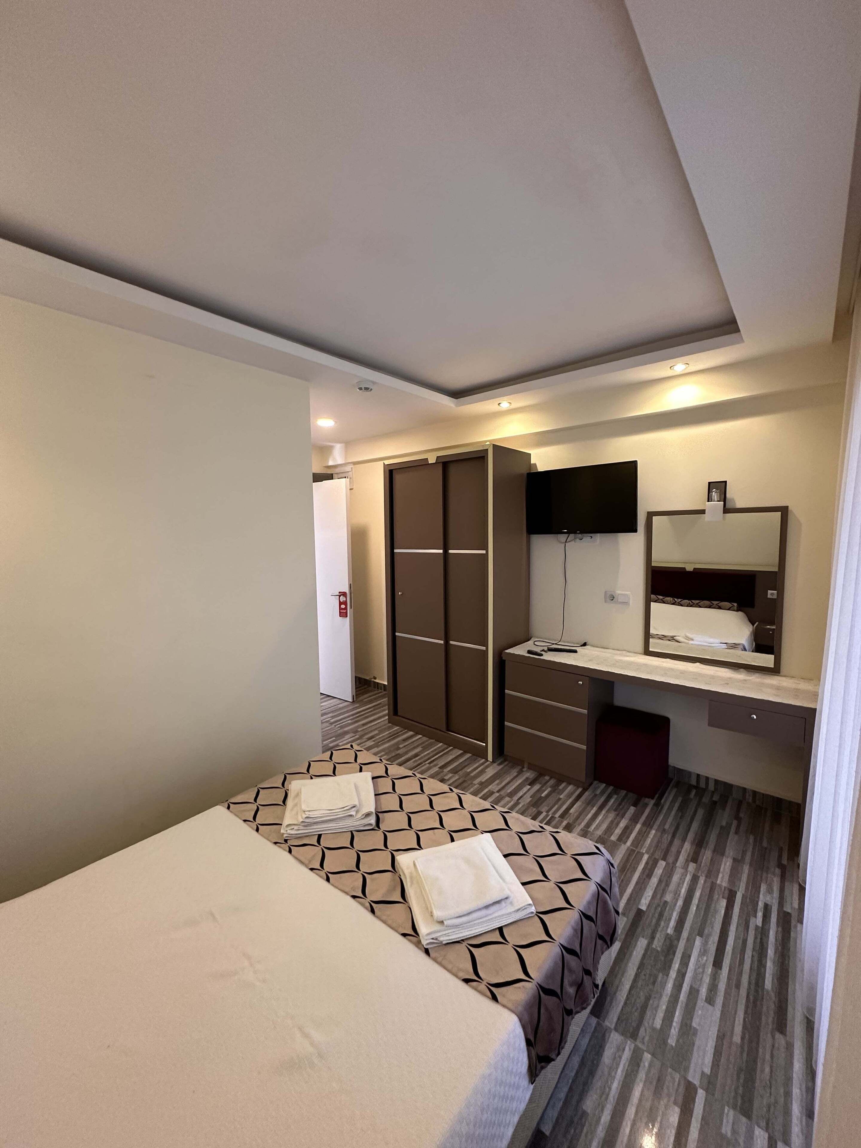 A hotel room with a bed, a wardrobe, a vanity with a mirror, and a small desk.
