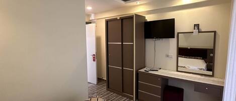 A hotel room with a bed, a wardrobe, a vanity with a mirror, and a small desk.