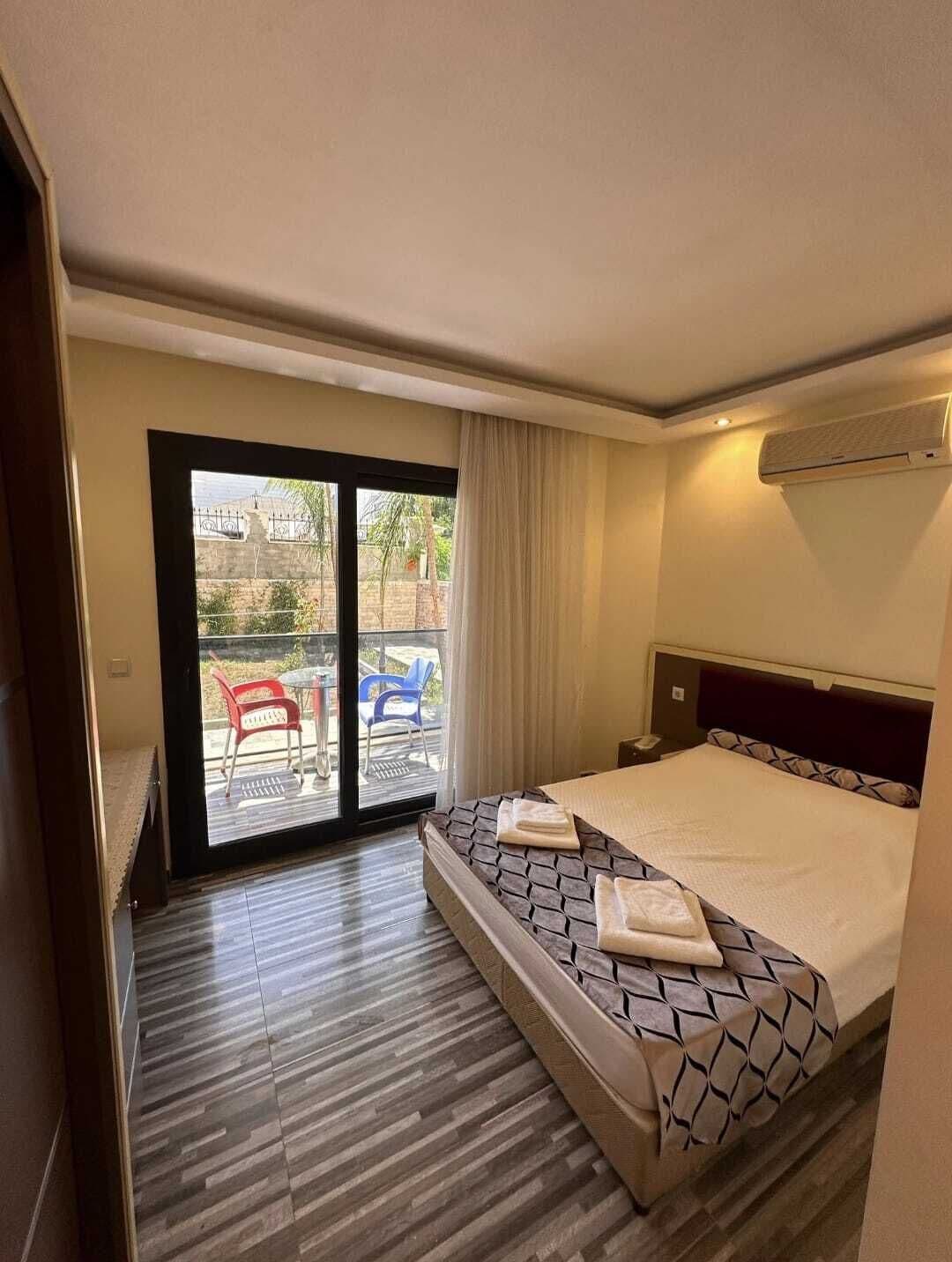 A hotel room with a bed, a desk, a chair, and a sliding glass door leading to an outdoor area.