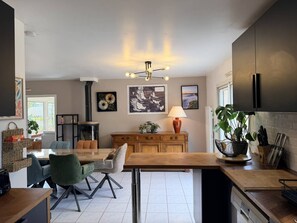 A modern kitchen with a dining area, featuring a central island, wooden cabinets, and a built-in stove. - Maison 8px, jacuzzi, jardin, 15 min à pied plage (QUIBERON)