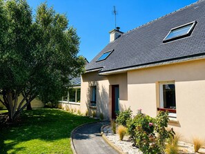 Ein modernes Haus mit geneigtem Dach, einem sichtbaren Schornstein und einem Weg zum Eingang.
