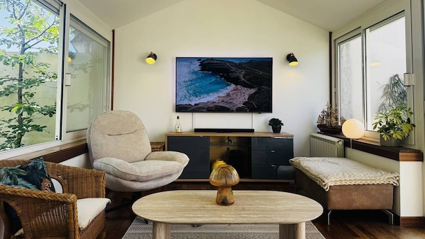Ein modernes Wohnzimmer mit einem großen Flachbildfernseher, einem bequemen Sessel, einem kleinen Tisch und einer Bank.