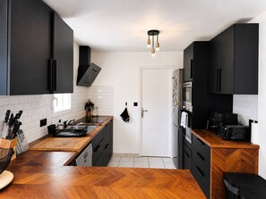 A modern kitchen with black cabinets, a wooden countertop, a built-in oven, and a coffee machine. - Maison 8px, jacuzzi, jardin, 15 min à pied plage (QUIBERON)