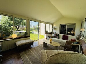 A spacious living room with a large window, a sofa, a coffee table, and a fireplace. - Maison 8px, jacuzzi, jardin, 15 min à pied plage (QUIBERON)