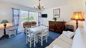 A living room with a sofa, dining table, chairs, a chandelier, a TV, a cabinet, and a lamp. - QUIBERON - 2 rooms - 55m2 - Sea view (QUIBERON)