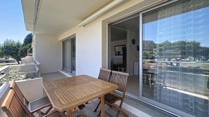 A balcony with a wooden table and chairs, a sliding glass door leading to an indoor area, and a view of a parking lot and buildings. - QUIBERON - 2 rooms - 55m2 - Sea view (QUIBERON)