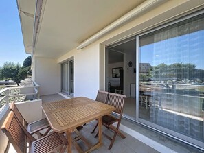 A balcony with a wooden table and chairs, a sliding glass door leading to an indoor area, and a view of a parking lot and buildings. - QUIBERON - 2 rooms - 55m2 - Sea view (QUIBERON)